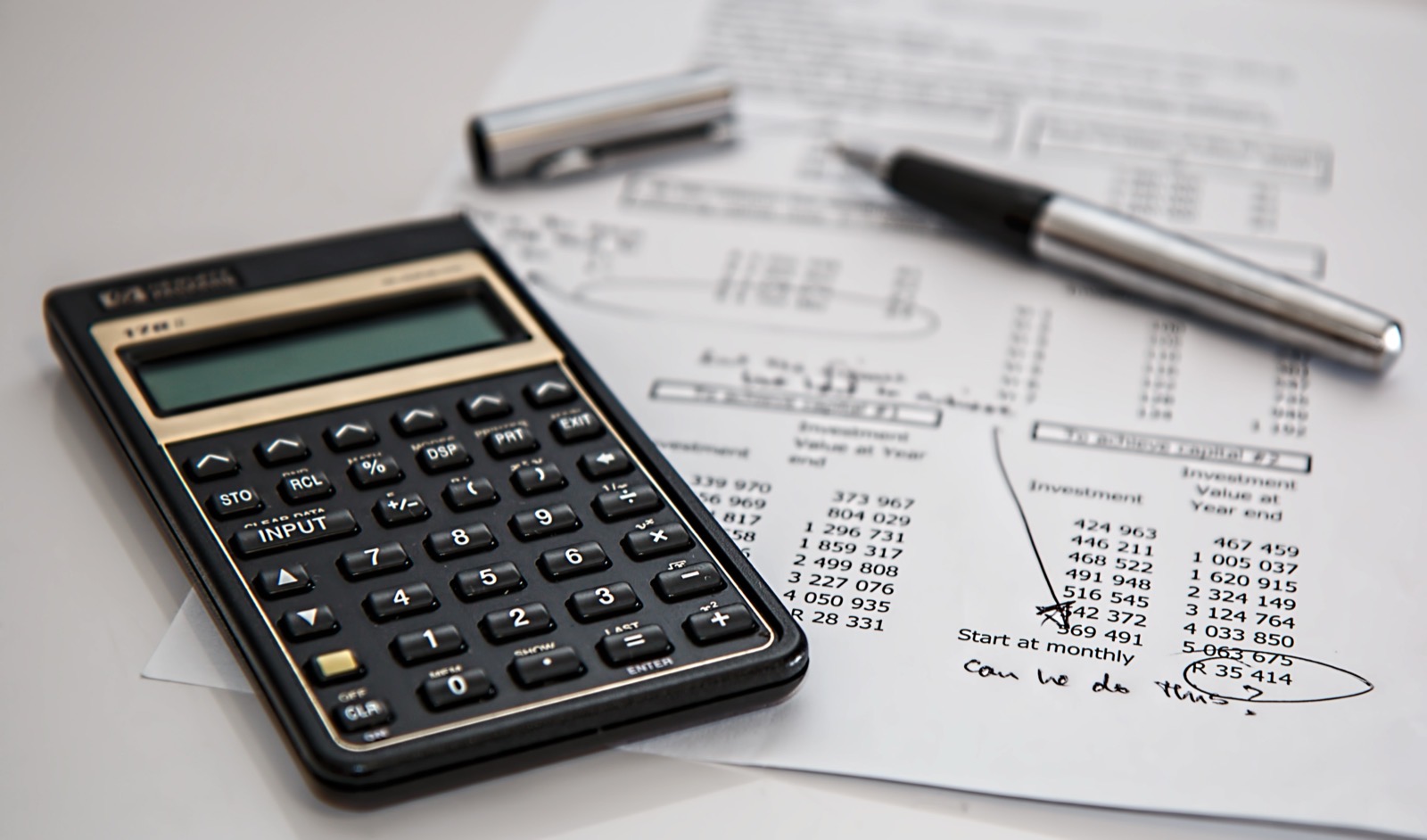Calculator and pen on a financial document with numbers and hand-written notes. The paper shows calculations circled for review.